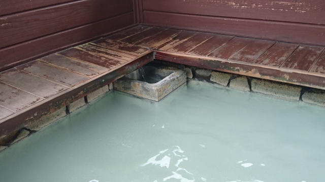 Milky white onsen water in a wooden bath, with hot spring water flowing from a spout