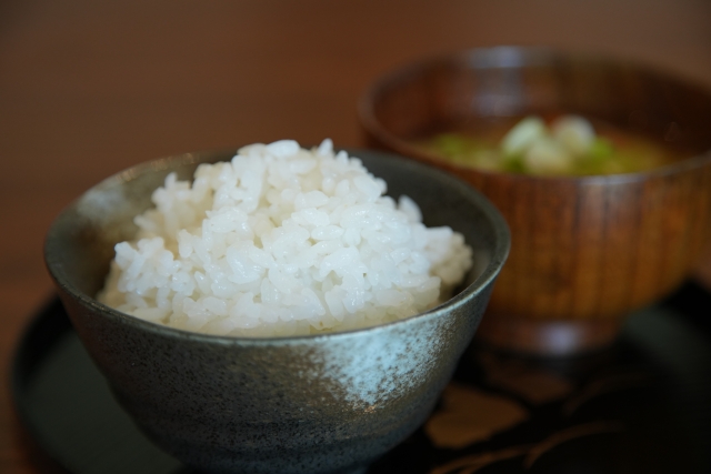 A bowl of freshly steamed Japanese rice served with miso soup in the background.
