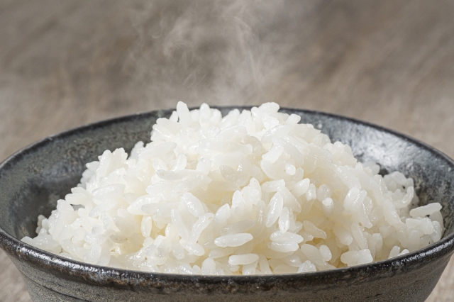 A bowl of freshly cooked Japanese rice with glossy, moist grains and steam rising from the surface.