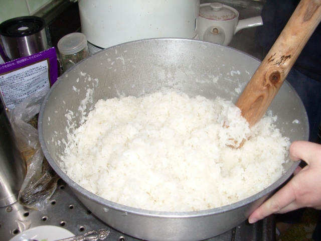 Cooked glutinous rice being mashed in a large bowl to make ohagi