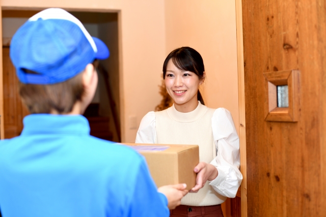 A delivery worker handing a package to a resident at the entrance of a Japanese home.
