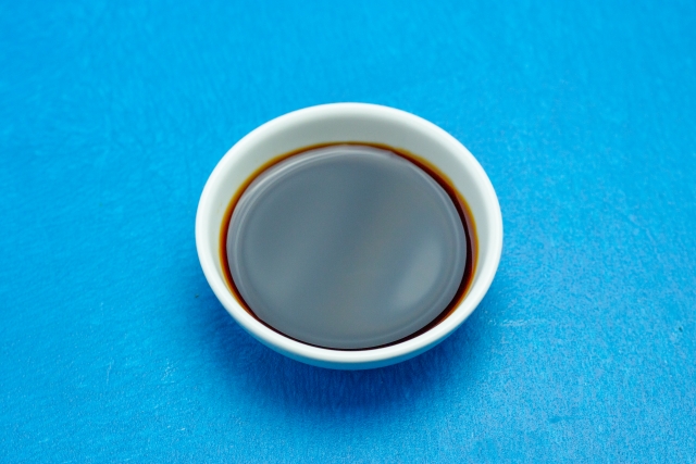 A small bowl of dark tamari soy sauce on a blue background