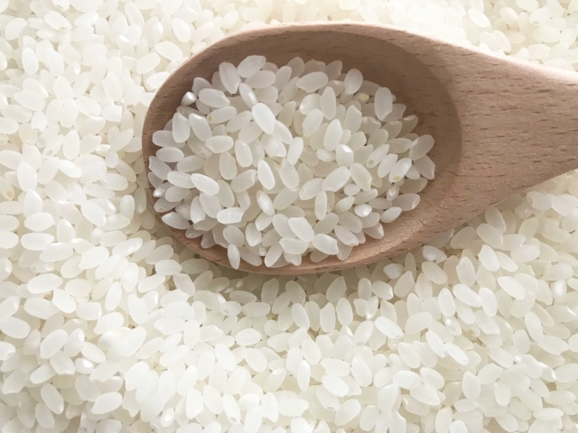 A close-up of uncooked Japanese short-grain rice in a wooden spoon.