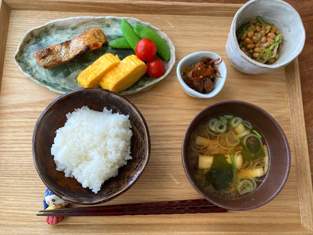 A Japanese-style breakfast tray with rice, miso soup, grilled fish, tamagoyaki, natto, and small side dishes.