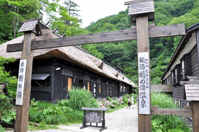 Entrance gate to a traditional ryokan in Nyuto Onsen with thatched-roof buildings and forested hills