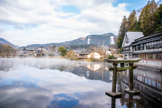 Steamy river in an onsen town with a torii gate by the water and mountains in the background