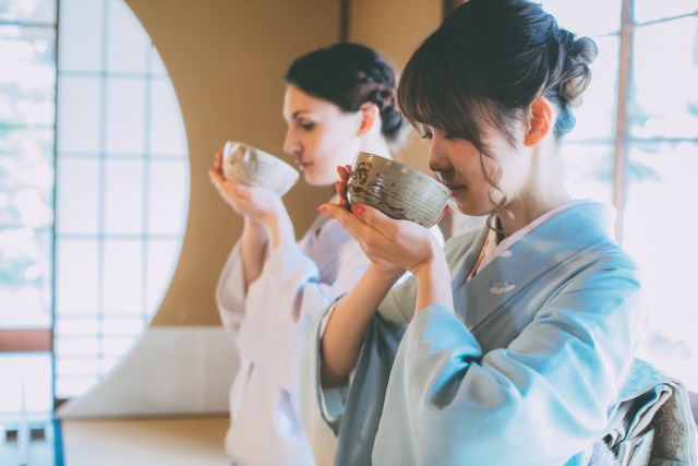 Two guests in kimono holding tea bowls close to their faces as they savor the aroma of matcha