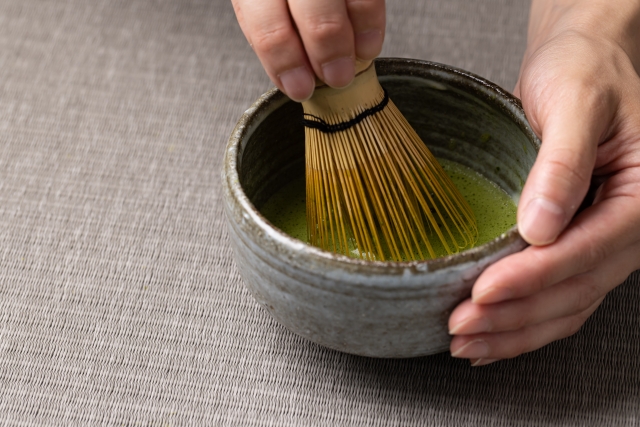 Matcha being whisked in a tea bowl with a bamboo chasen.
