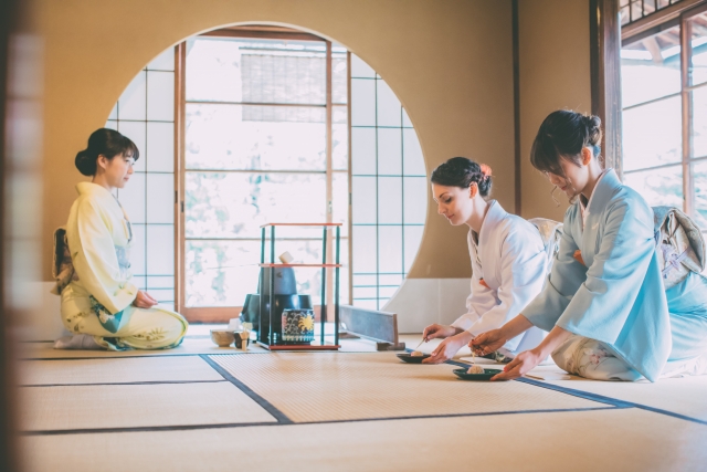 Tea ceremony in a tatami room with a host preparing matcha and guests seated in kimono