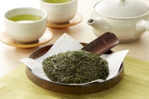 Sencha tea leaves with a Japanese teapot and cups of brewed green tea.
