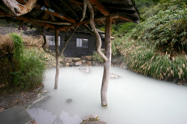 Rustic outdoor sulfur onsen with milky water under a wooden roof and posts