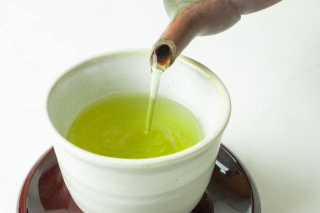 Sencha being poured into a white teacup, showing its bright green color.