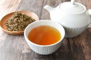 Hojicha tea with roasted tea leaves, a white teapot, and a cup of amber-colored tea.