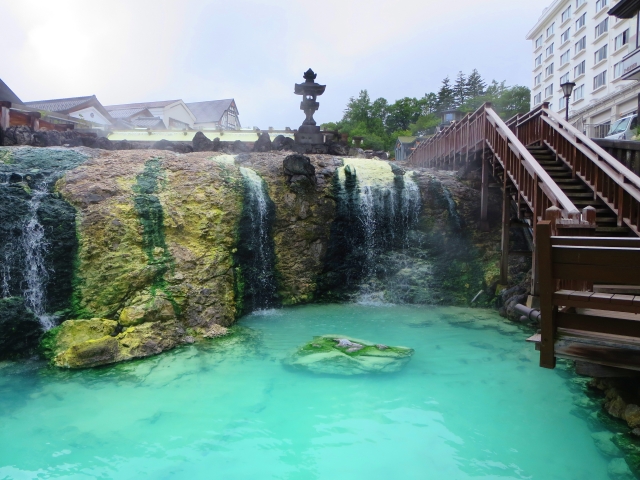Hot spring water cascading over rocks into a bright turquoise pool in Kusatsu