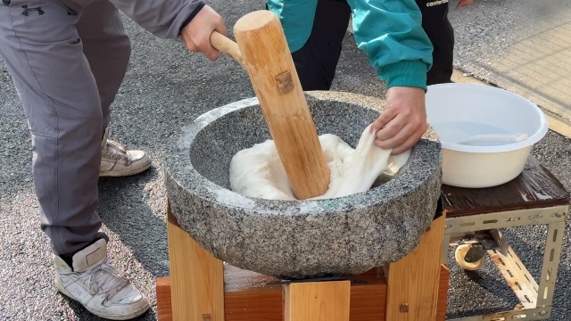 People making traditional Japanese mochi by pounding steamed glutinous rice in a stone mortar