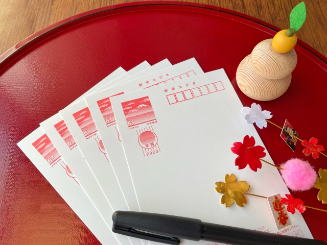 Blank Japanese nengajo postcards prepared for writing, with New Year decorations and a pen placed on a tray 