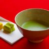 Bowl of matcha with two wagashi sweets on a red cloth background