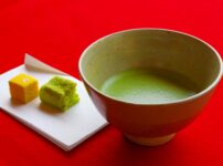 Bowl of matcha with two wagashi sweets on a red cloth background