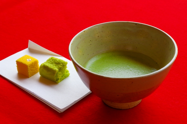 Bowl of matcha with two wagashi sweets on a red cloth background