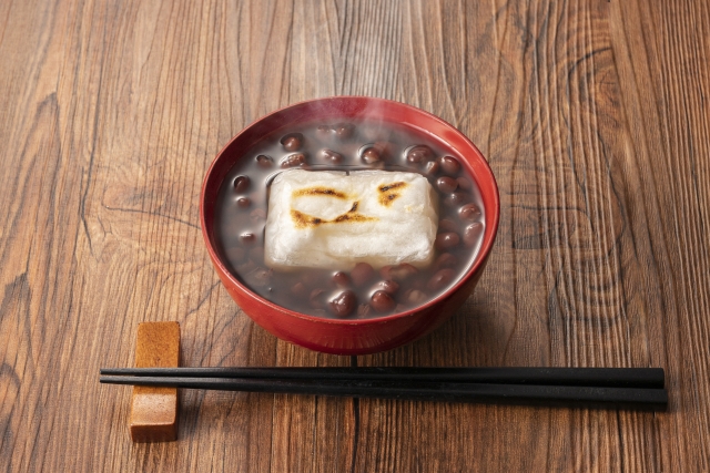 Oshiruko with grilled mochi in a red bowl on a wooden table