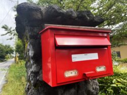 Red Japanese postbox used for mailing nengajo New Year greeting cards, standing beside a quiet residential road
