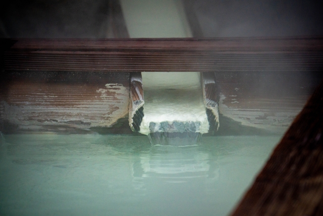 Hot spring water flowing into an onsen bath, with mineral deposits around the spout