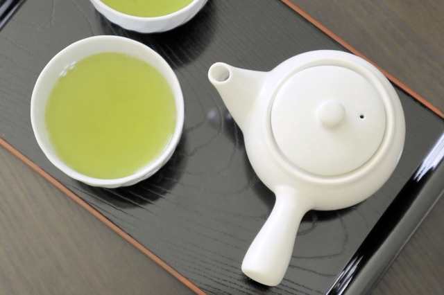 Sencha green tea served in a cup beside a white Japanese kyusu teapot.