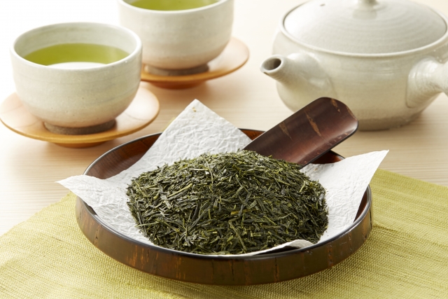 Sencha tea leaves with a Japanese teapot and cups of brewed green tea.