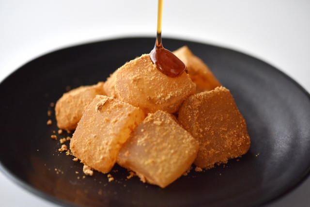 Warabi mochi coated with kinako and drizzled with kuromitsu on a black plate