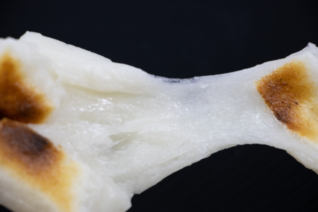 Grilled Japanese mochi stretching to show its soft, chewy, and elastic texture