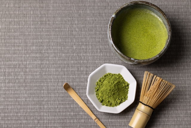 alt="Matcha powder with tea bowl and bamboo whisk on tatami mat"