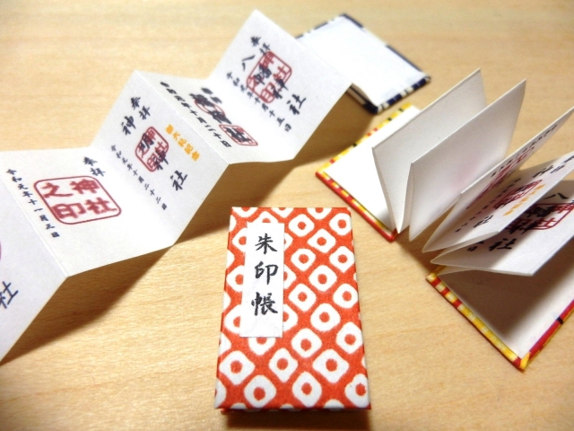 An open accordion-style goshuincho book showing beautiful Japanese calligraphy and red vermilion stamps from different shrines.