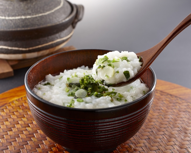 A spoonful of nanakusa-gayu showing soft rice porridge mixed with chopped green herbs.