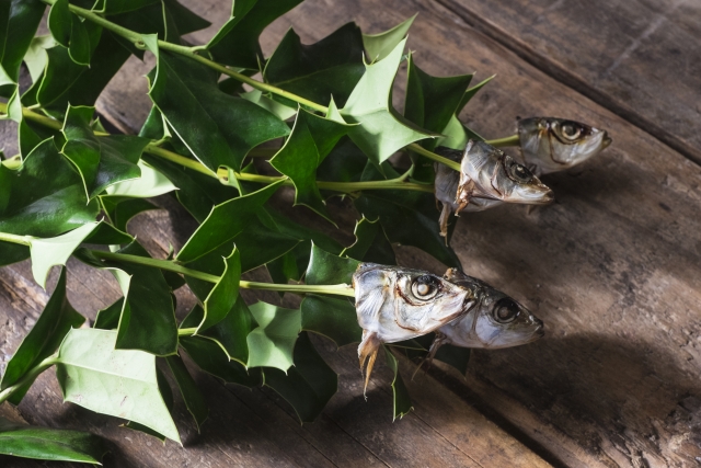 Hiiragi iwashi with several grilled sardine heads attached to holly leaves on a wooden surface