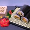 Setsubun items: roasted soybeans in a masu box, oni mask, and ehomaki sushi rolls