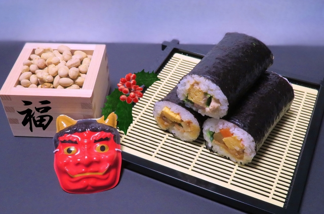 Setsubun items: roasted soybeans in a masu box, oni mask, and ehomaki sushi rolls