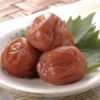 Three umeboshi (Japanese pickled plums) served on a small plate with a shiso leaf