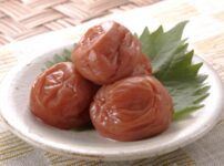Three umeboshi (Japanese pickled plums) served on a small plate with a shiso leaf