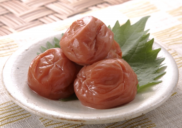Three umeboshi (Japanese pickled plums) served on a small plate with a shiso leaf