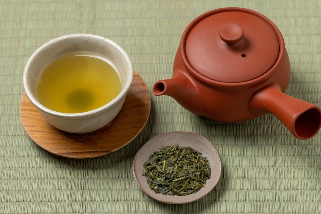 A traditional kyusu teapot and yunomi cups with loose Japanese green tea leaves