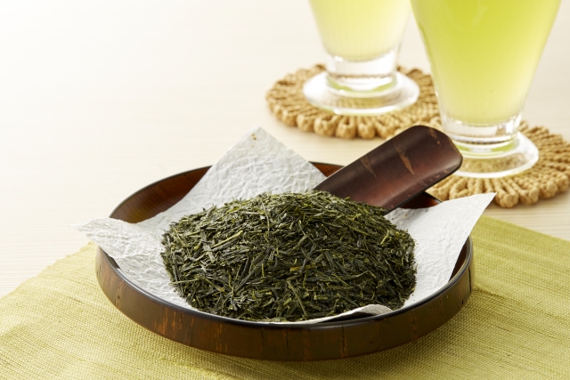 Loose green tea leaves placed beside a glass of chilled green tea