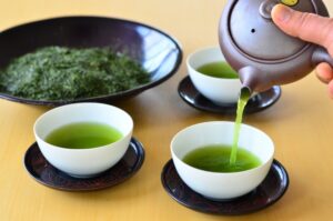 Deep green fukamushi-cha being poured from a Japanese teapot into small teacups