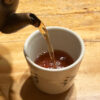 Hojicha being poured into a Japanese teacup, showing its warm amber-brown color