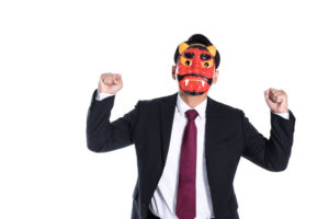 Man in a suit wearing a red oni mask, raising his fists against a white background