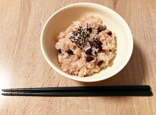 A bowl of sekihan topped with black sesame gomashio, showing the reddish glutinous rice and whole red beans.