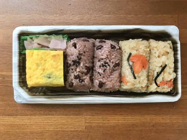 A prepared Japanese meal featuring sekihan rice, seasoned rice, tamagoyaki, and pickles sold in a supermarket.
