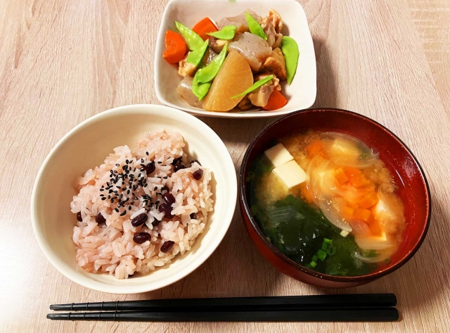A traditional Japanese meal with sekihan, miso soup, and simmered vegetables served on a home dining table.