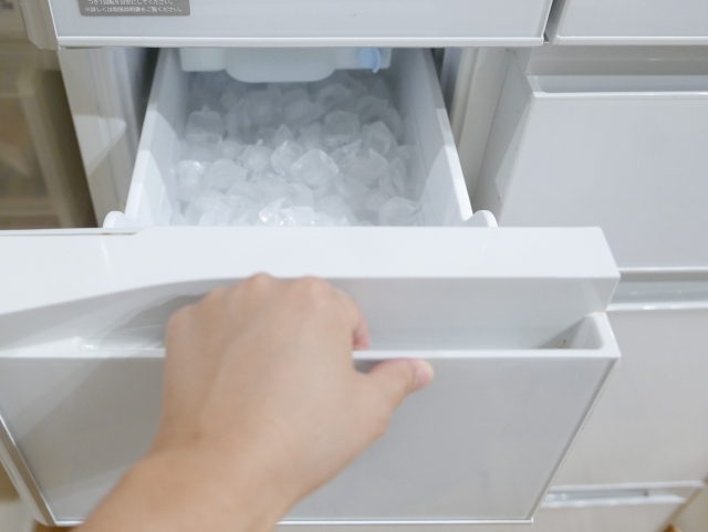 Hand opening a freezer drawer filled with ice cubes
