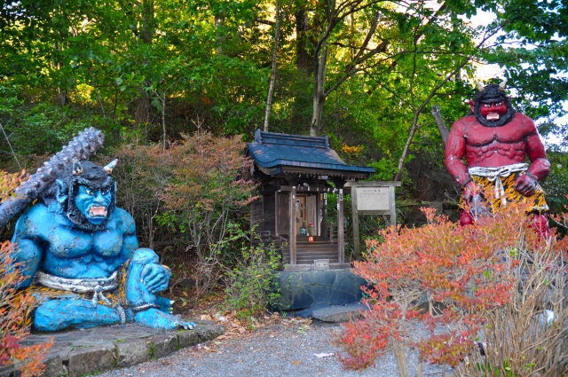 Blue and red oni statues standing near a small shrine, representing different forms of fear in Japanese folk belief