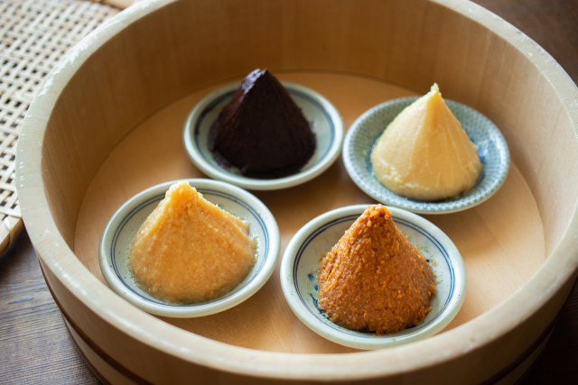 Four varieties of Japanese miso paste, ranging from pale white to deep red, displayed in small dishes.
